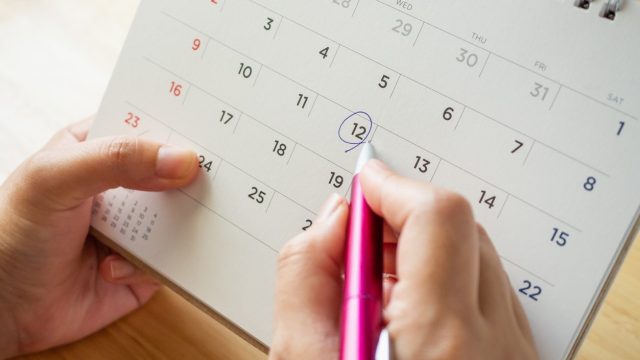calendar page with female hand holding pen on desk table